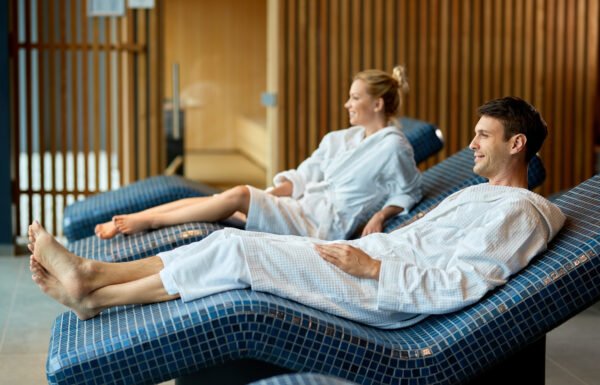 Smiling couple in bathrobes relaxing on lounge chairs at the spa